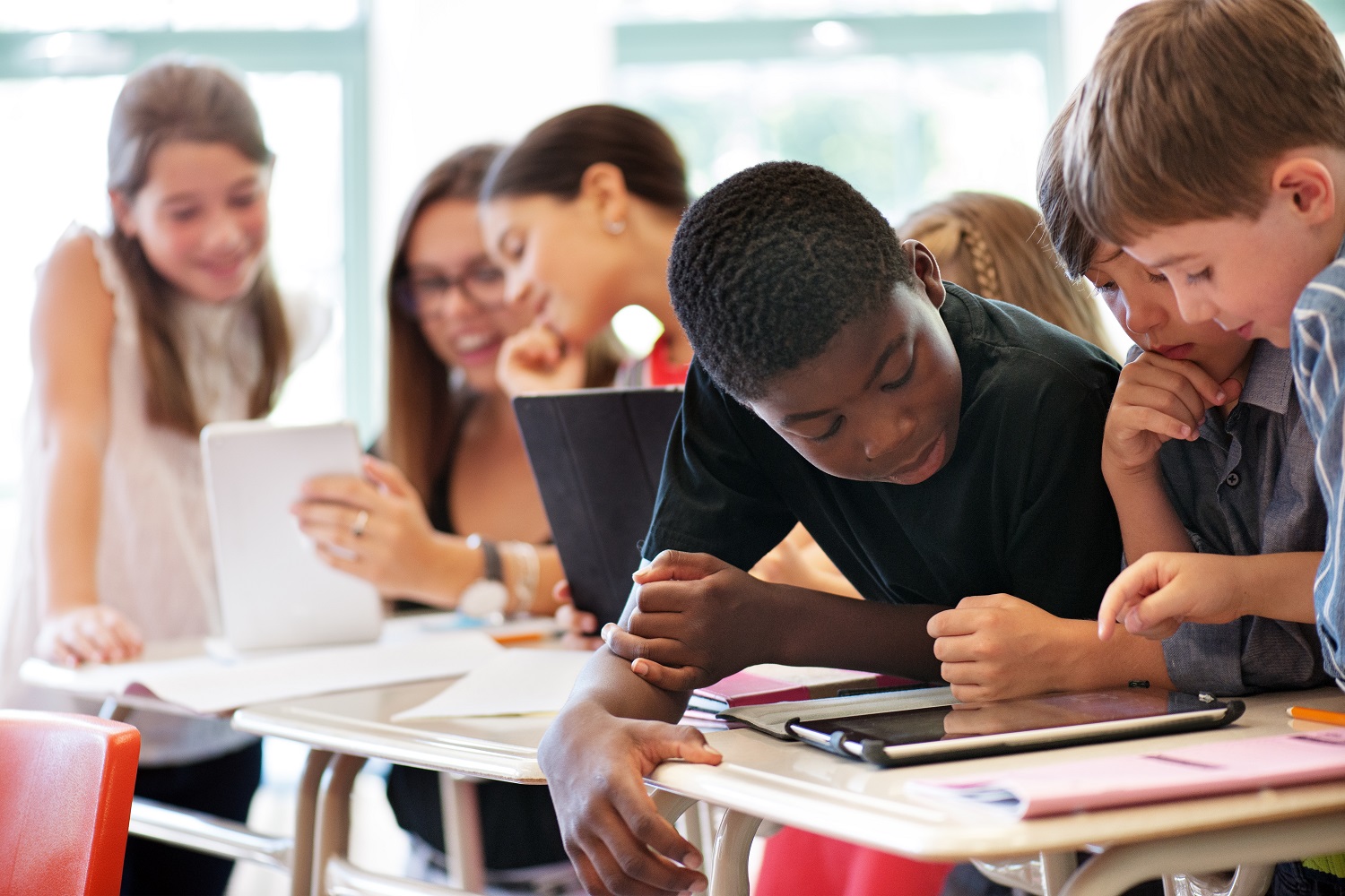 Schülerinnen und Schüler blicken auf Tablets, die vor ihnen auf dem Tisch liegen.