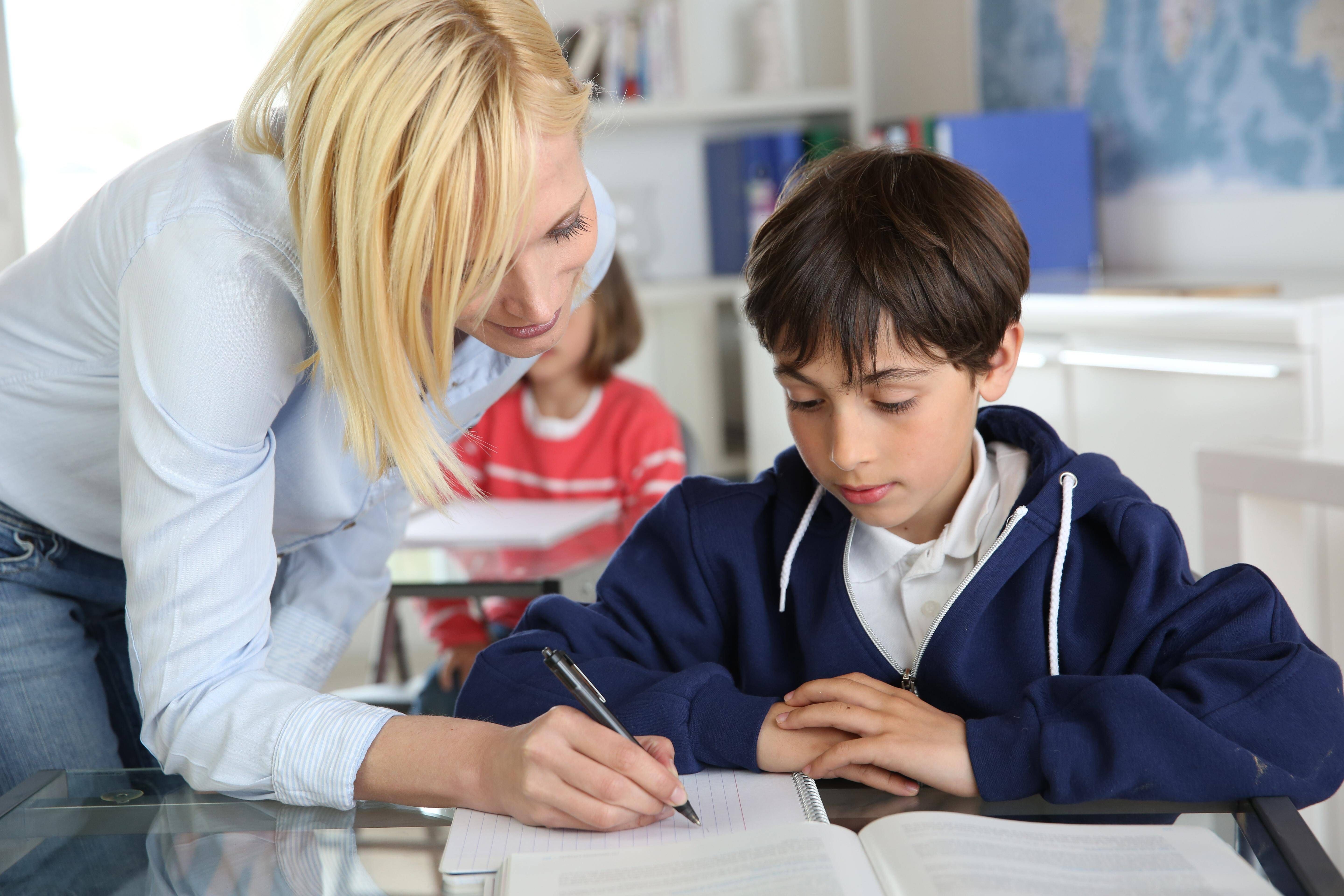Eine Lehrerin beugt sich im Unterricht helfend über einen Schüler. Eine Lehrerin beugt sich im Unterricht helfend über einen Schüler.