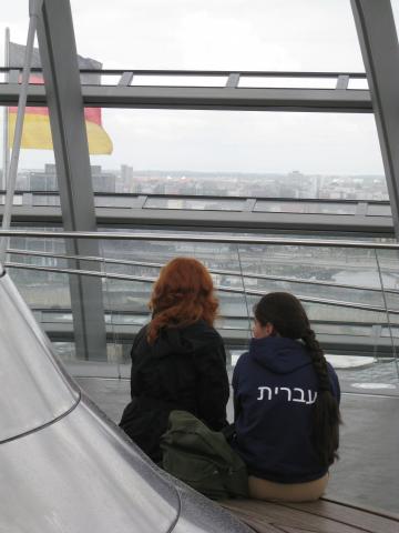 Rückansicht zweier Mädchen, die in der Reichstagskuppel auf Stufen nebeneinander sitzen. Eines der Mädchen trägt ein Sweatshirt mit hebräischen Schriftzeichen., 