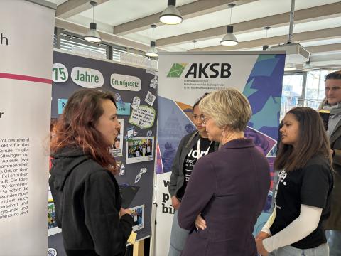 Schulministerin Feller steht mit Schülerinnen und Schülern vor einem Stand der Regionalen Lernstatt NRW zu 75 Jahre Grundgesetz.