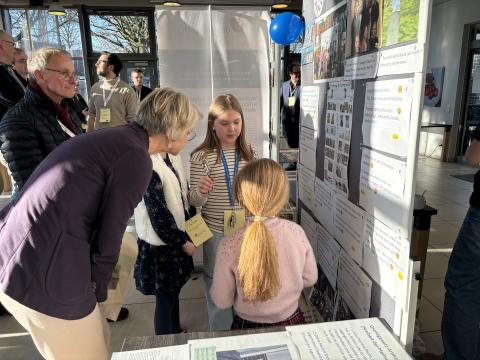 Schulministerin Feller betrachtet mit drei Schülerinnen den Stand ihrer Schule bei der Regionalen Lernstatt NRW.