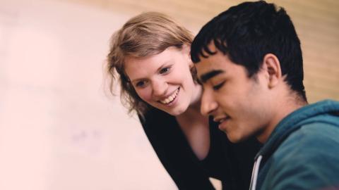 Junge Lehrerin beugt wendet sich einem Schüler im Teenager-Alter zu.