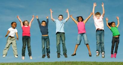 SiebenSieben Kinder unterschiedlichen Alters und verschiedener Herkunft springen in Jeans und T-Shirt vor sommerlich blauem Himmel auf einer gemähten Wiese mit erhobenden Armen in die Luft