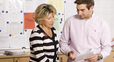 Eine Lehrerin und ein Lehrer unterhalten sich über ein Dokument, in das beide blicken.