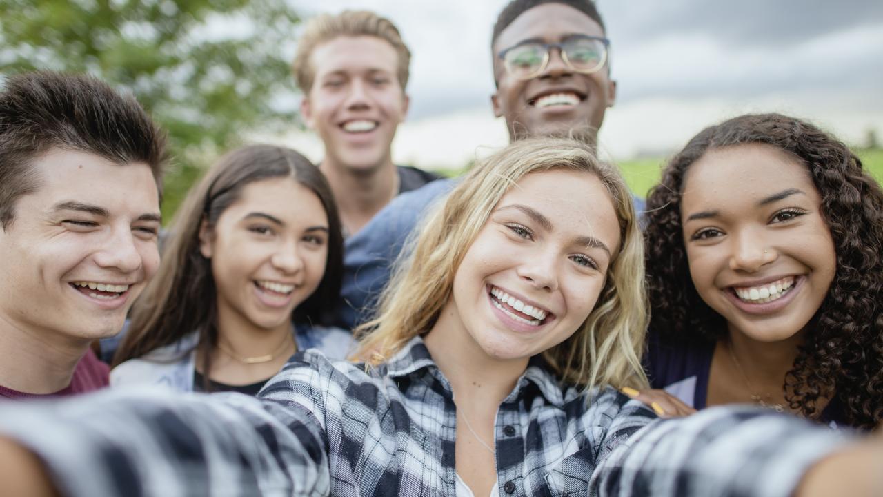Selfie-Perspektive auf mehrere junge Menschen, die sich lächelnd zum Foto gruppiert hat.