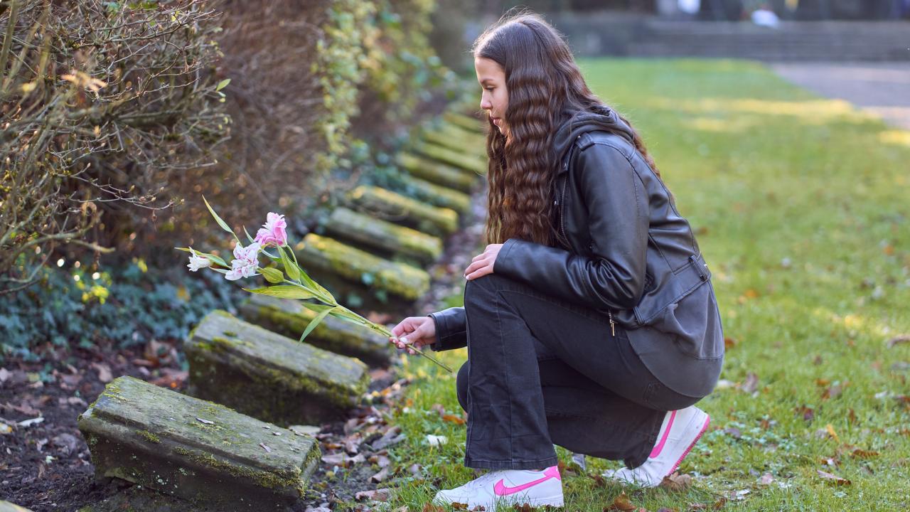 Eine Schülerin legt Blumen auf einem Grab einer Gedenkstätte nieder.