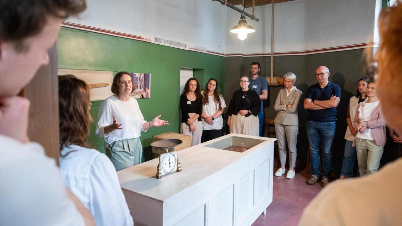 Ministerin Feller sowie Lehramtsanwärterinnen und -anwärter stehen in einem Raum des Humberghauses und hören einer Führung zu.