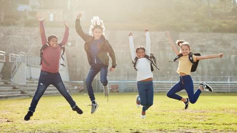 Eine Gruppe Kinder springt auf einer Wiese in die Luft.