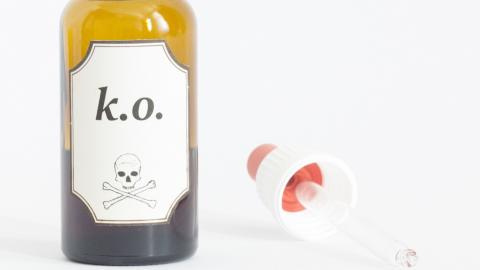 Eine Pipette liegt neben einem geöffneten Glasfläschen mit einem Etikett mit der Aufschrift "k.o." sowie einem Totenkopf.