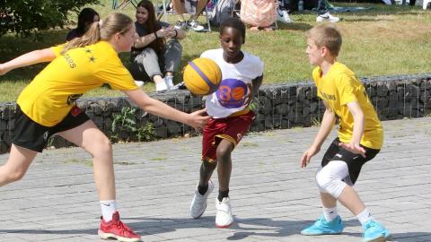 Zwei Jungen und ein Mädchen spielen Streetbasketball.