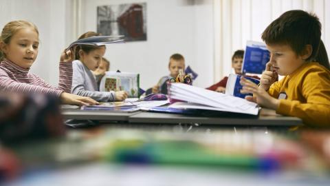 Grundschülerinnen und Grundschüler sitzen während des Unterrichts vor aufgeschlagenen Büchern, lesen und arbeiten.