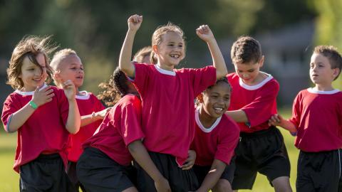 Kinder in Sport-Trikots stehen jubelnd zusammen.