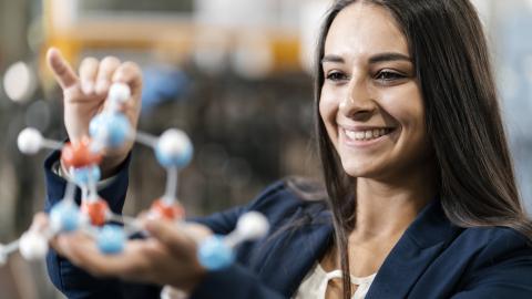 Eine junge Frau betrachtet ein naturwissenschaftliches Modell in ihren Händen..