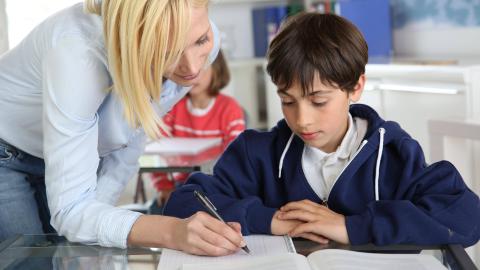 Eine Lehrerin beugt sich im Unterricht helfend über einen Schüler.