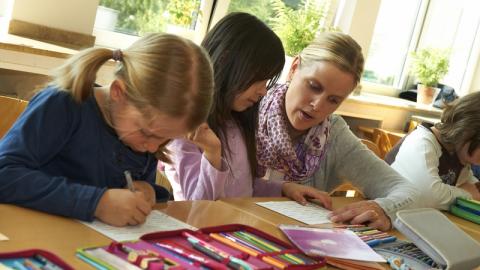 Eine Lehrerin sitzt zwischen Grundschülerinnen und erklärt etwas.