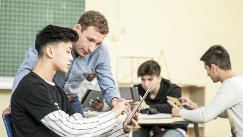 Schüler und Lehrer blicken gemeinsam auf ein Tablet.