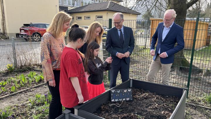 An der Pestalozzischule Mülheim stehen Janina Hietzschold (stellvertretende Schulleiterin), Klassensprecherin Zula, Schulsprecherin Emma, Schulleiterin Julia Friedrichs, Sts Dr. Mauer, Martin Teuber, Referatsleiter 33 an einem Hochbeet.