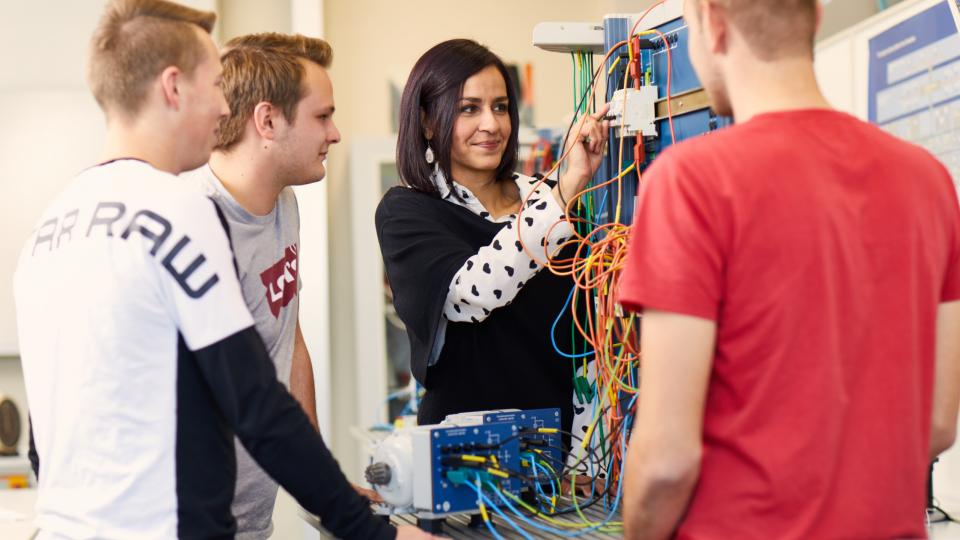 Lehrerin erklärt Schülern im naturwissenschaftlichen Unterricht eine eletronische Aparatur.