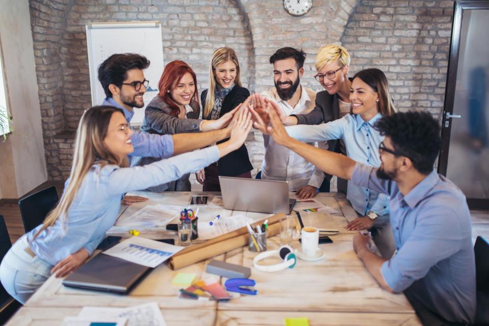 Gruppe Erwachsener lehnt sich über einen Arbeitstisch und bringt die Hände in der Mitte zusammen. Gruppe Erwachsener lehnt sich über einen Arbeitstisch und bringt die Hände in der Mitte zusammen.