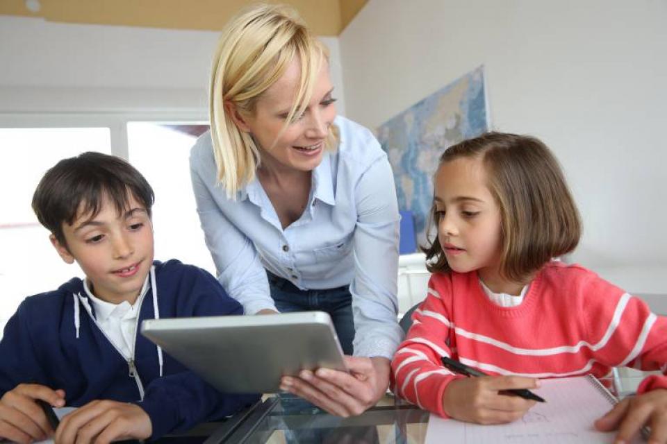 Lehrerin erklärt zwei Schülern Unterrichtsstoff mithilfe eines mobilen Endgerätes Lehrerin erklärt zwei Schülern Unterrichtsstoff mithilfe eines mobilen Endgerätes