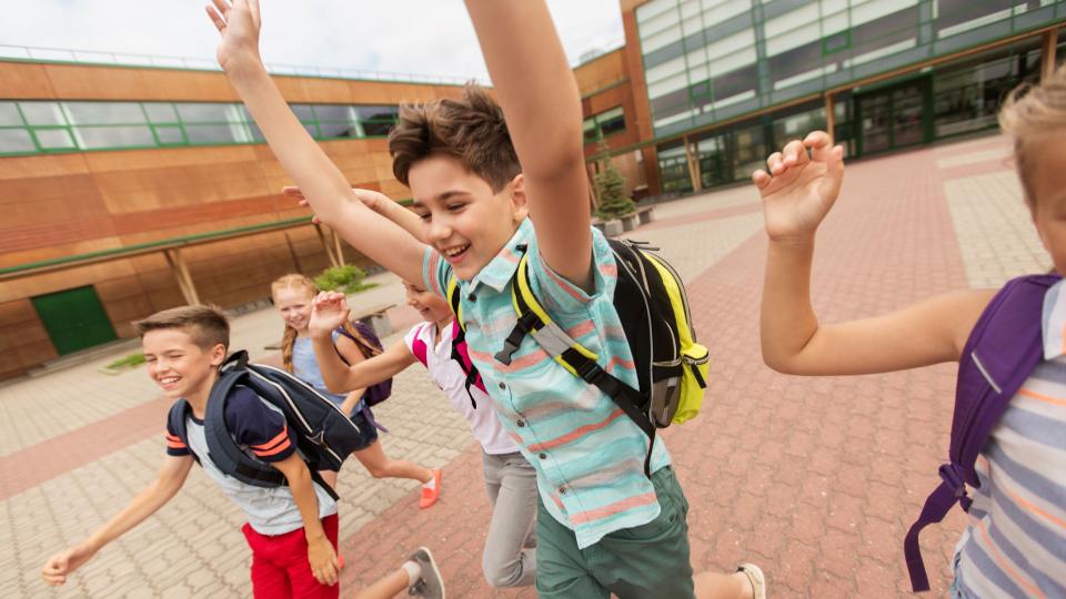 Schülerinnen und Schüler laufen fröhlich über einen Schulhof.