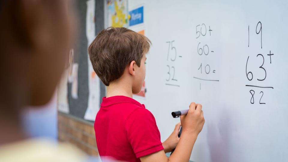Grundschüler löst eine Mathematikaufgabe an der Tafel.