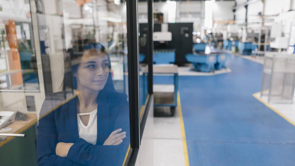 Eine Frau blickt durch eine Glasscheibe in eine High-Tech-Produktionshalle. Eine Frau blickt durch eine Glasscheibe in eine High-Tech-Produktionshalle.