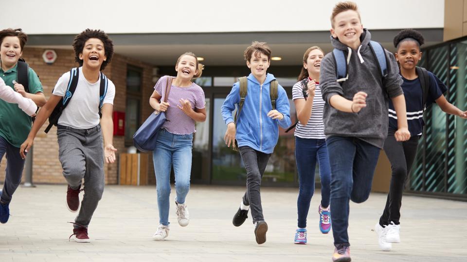 Schüler laufen lachend aus Schulgebäude.