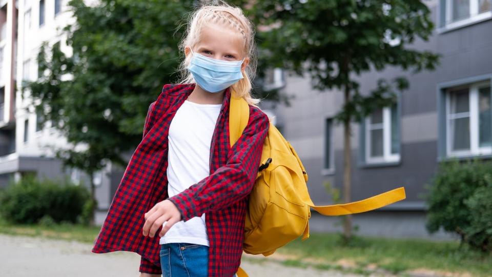 Mädchen mit Mund-Nasen-Schutz läuft mit einem Rucksack über der Schulter. Mädchen mit Mund-Nasen-Schutz läuft mit einem Rucksack über der Schulter.