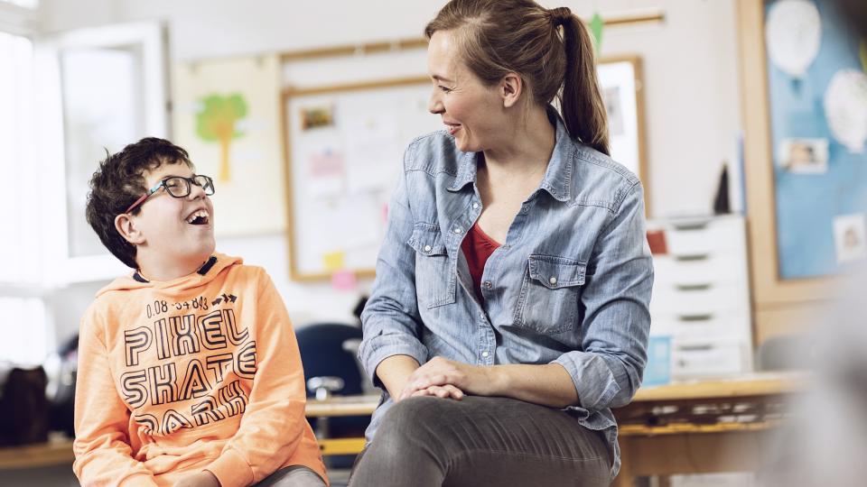 Lehrerin und Förderschulkind lächeln sich an.