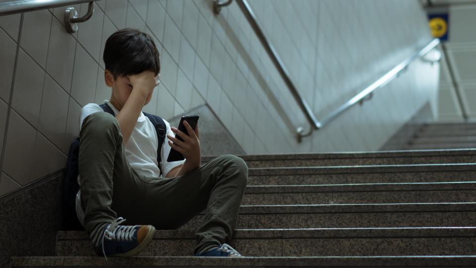 Junge sitzt mit seinem Smartphone in der Hand auf einer Treppe