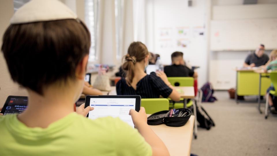 Eine Junge mit Kippa schaut im Unterricht auf sein iPad