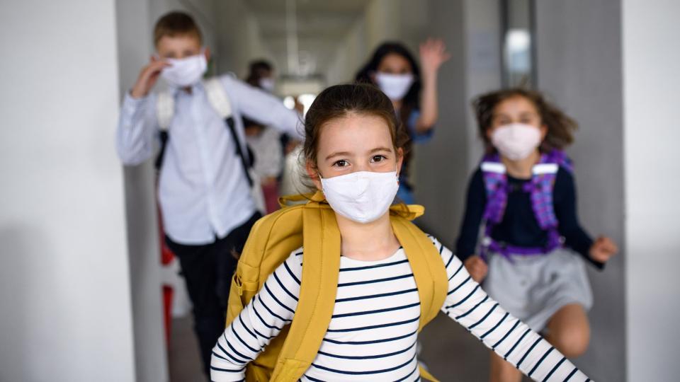 Eine Gruppe Schülerinnen und Schüler läuft Alltagsmasken tragend einen Schulflur entlang. Eine Gruppe Schülerinnen und Schüler läuft Alltagsmasken tragend einen Schulflur entlang.