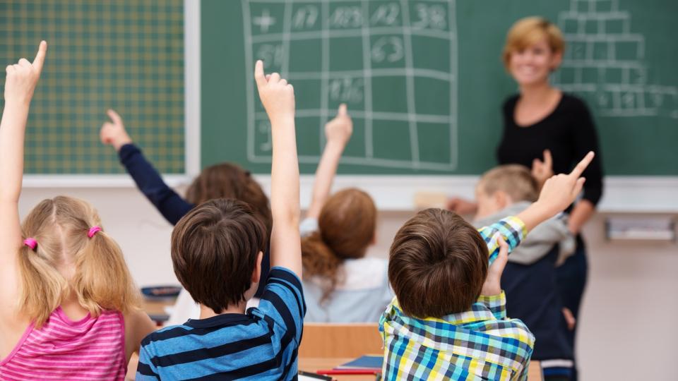 Grundschülerinnen und -schüler melden sich, im Hintergrund eine Tafel mit Rechenaufgaben Grundschülerinnen und -schüler melden sich, im Hintergrund eine Tafel mit Rechenaufgaben