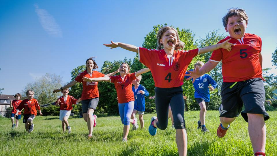 Kinder und Jugendliche in Sportkleidung rennen über eine Wiese