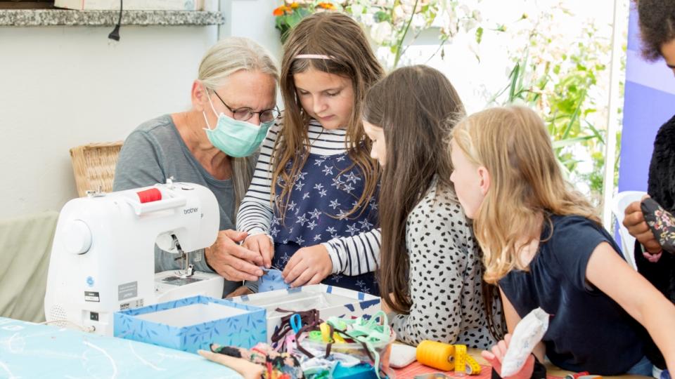 Drei Kinder und eine Frau sitzen gemeinsam an einer Nähmaschine.