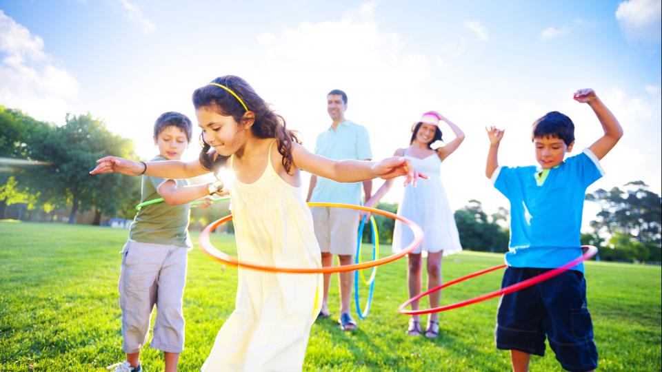 Eine Familie spielt auf der Wiese mit Hula Hoop-Reifen