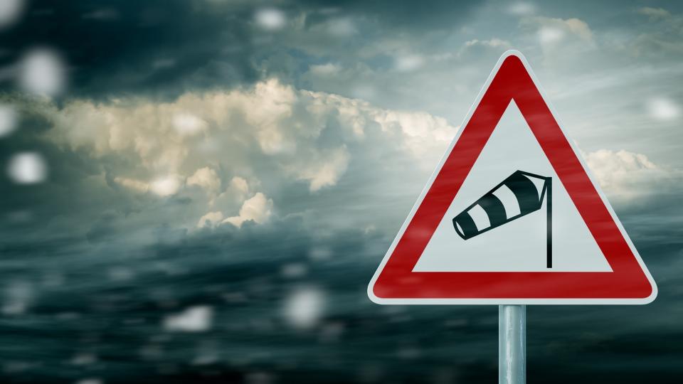 Sturm-Warnschild (rotes Dreieck mit einem gefüllten Windsack an einer Stange) vor stürmischem Wolkenhimmel. Sturm-Warnschild (rotes Dreieck mit einem gefüllten Windsack an einer Stange) vor stürmischem Wolkenhimmel.