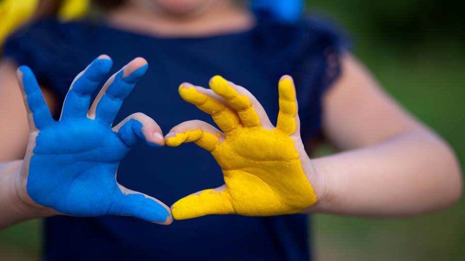 Blau und gelb bemalte Hände formen ein Herz