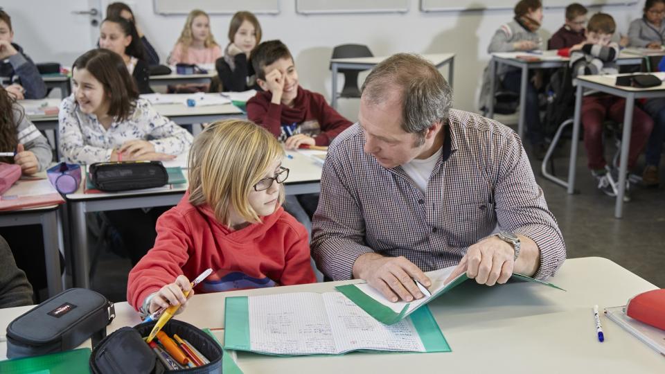 Unterrichtssituation: Ein Lehrer sitzt neben einem Schüler und erklärt ihm etwas. Unterrichtssituation: Ein Lehrer sitzt neben einem Schüler und erklärt ihm etwas.