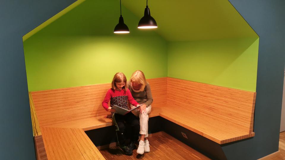 Eine Frau und ein Mädchen sitzen auf einer Eckbank und lesen gemeinsam ein Buch. Eine Frau und ein Mädchen sitzen auf einer Eckbank und lesen gemeinsam ein Buch.