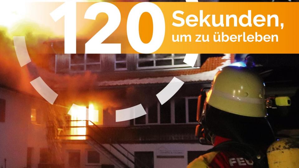 Ein Feuerwehrmann steht vor einem brennenden Haus.