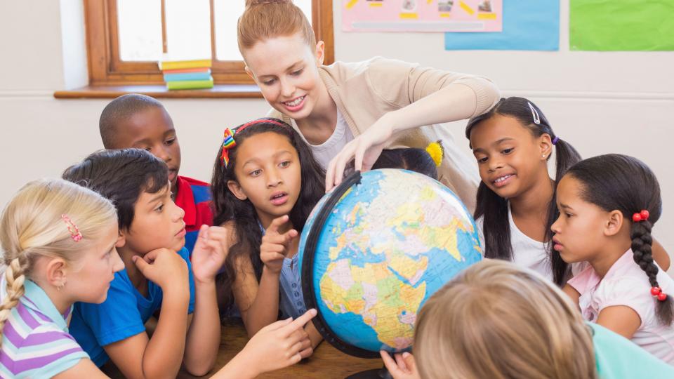 Eine Schülergruppe betrachtet zusammen mit einer Lehrerin einen Globus.