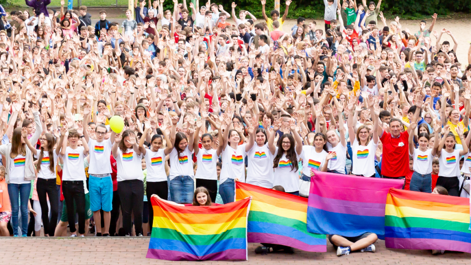 Die ganze Schulgemeinde des GKGE Troisdorf steht mit Regenbogenflaggen auf dem Schulhof. Die ganze Schulgemeinde des GKGE Troisdorf steht mit Regenbogenflaggen auf dem Schulhof.