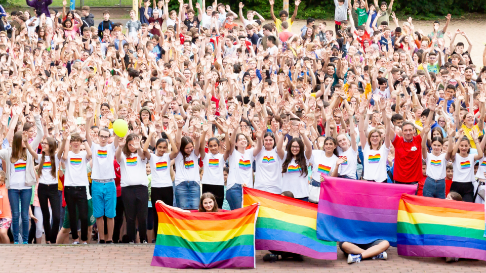 Die ganze Schulgemeinde des GKGE Troisdorf steht mit Regenbogenflaggen auf dem Schulhof.