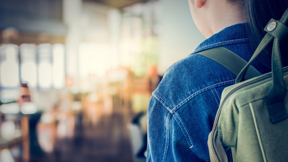 Rückansicht eines Mädchens mit Rucksack vor einem Klassenraum.