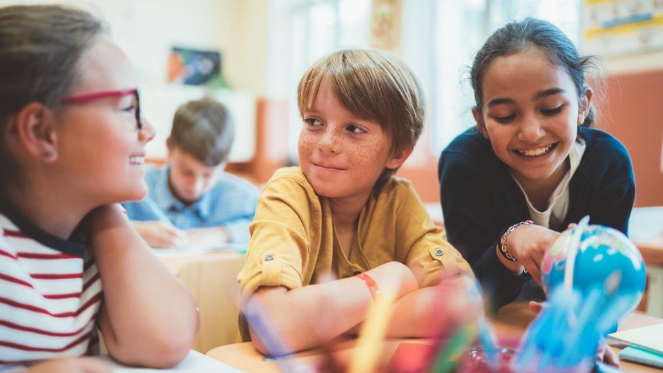 Grundschülerinnen und Grundschüler sitzen an einem Tisch im Unterricht und bearbeiten gemeinsam eine Aufgabe.