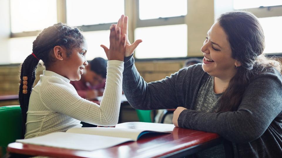 Schülerin und Lehrerin berühren ihre Hände in einer "High Five"-Geste. Beide lächeln dabei. Schülerin und Lehrerin berühren ihre Hände in einer "High Five"-Geste. Beide lächeln dabei.