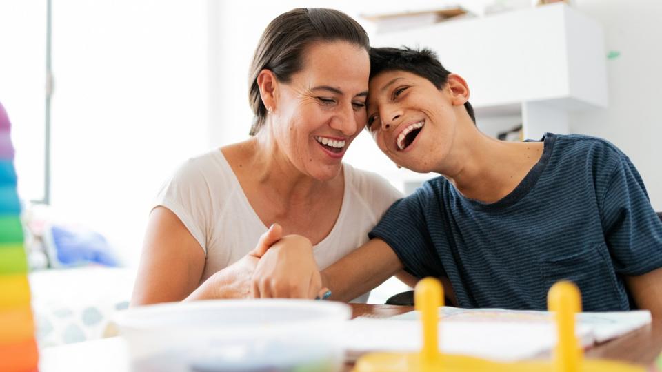 Ein Kind mit Behinderungen und seine Mutter sitzen an einem Tisch mit Lernmaterialien. Ein Kind mit Behinderungen und seine Mutter sitzen an einem Tisch mit Lernmaterialien.