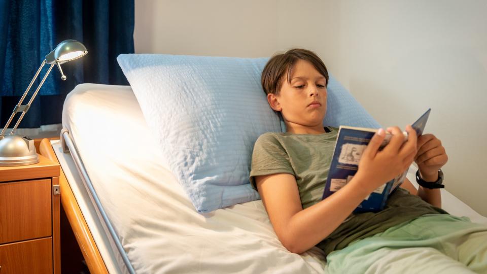 Ein Junge liegt in einem Krankenbett und liest in einem Buch